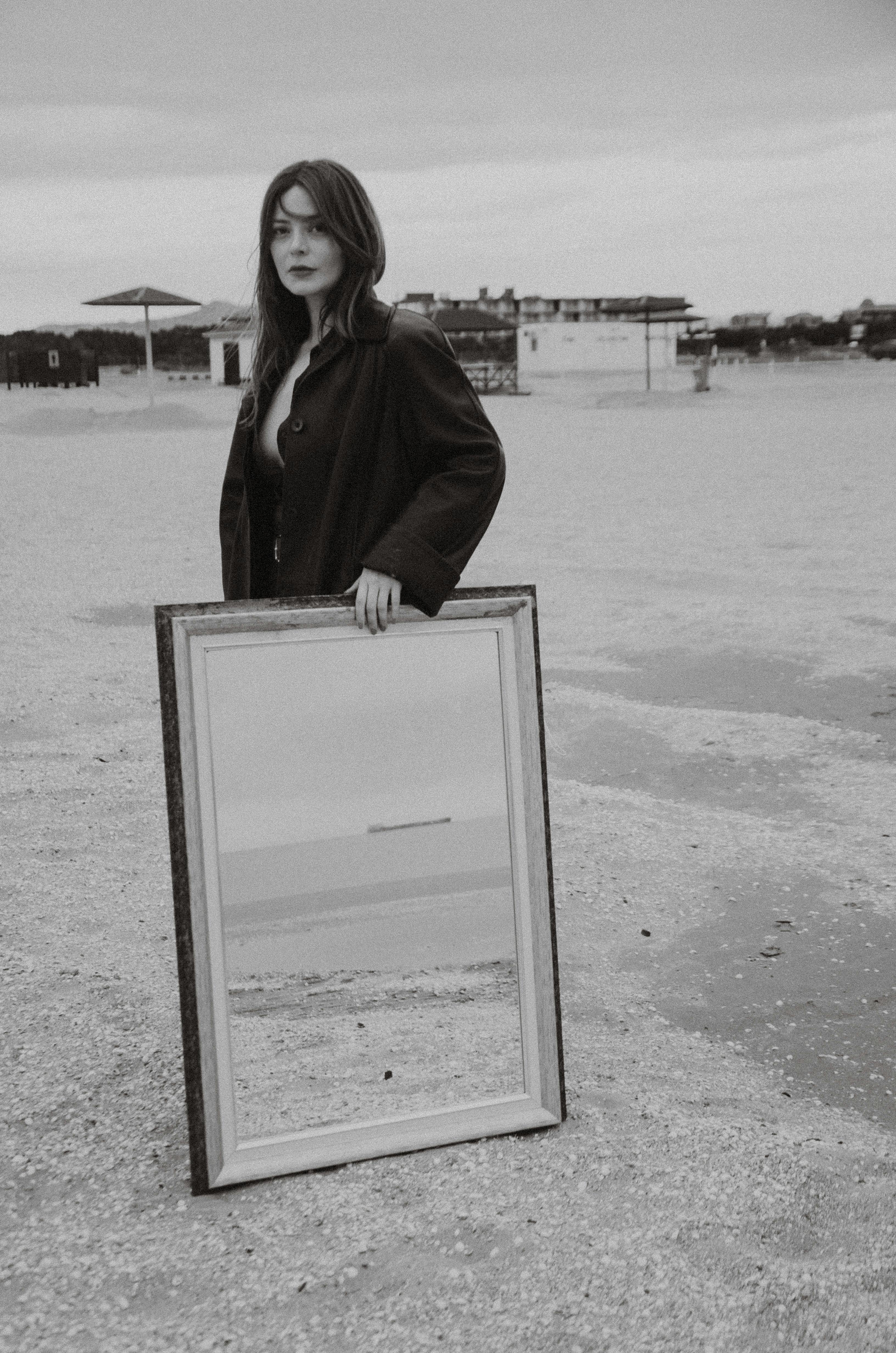 Artistic black and white photo of a woman holding a mirror on the beach.