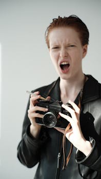 Person with camera expressing emotion in a studio setting, leather jacket, cigarette