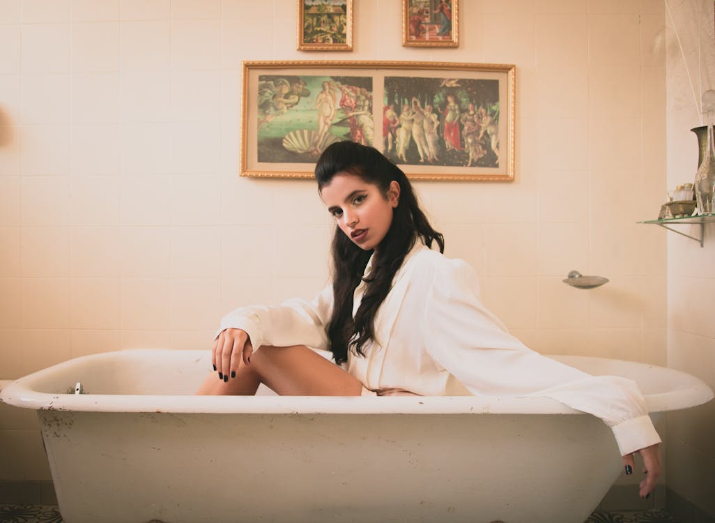 Woman in White Long-sleeved Shirt Sitting on White Ceramic Bathtub