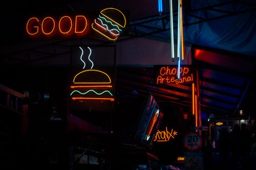 Free Vibrant neon signs at an urban night market, featuring a burger and artisan drink sign. Stock Photo