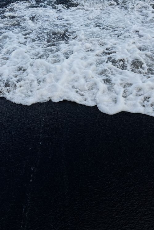 Free Waves of sea foam gently wash over the black sand beach in Hilo, Hawaii. Stock Photo