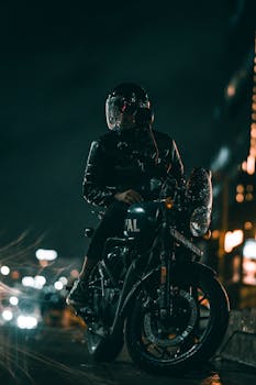 Motorcyclist wearing helmet on bike in rainy Hyderabad night, vibrant city street scene.