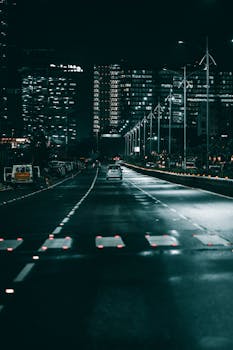 Dramatic city street scene at night, highlighting urban traffic and illuminated skyscrapers.