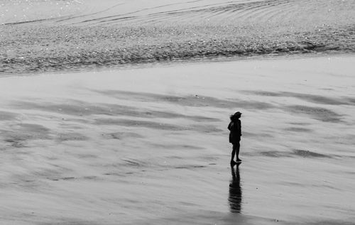 Free A lone person walks on a shimmering wet beach, captured in black and white. Stock Photo