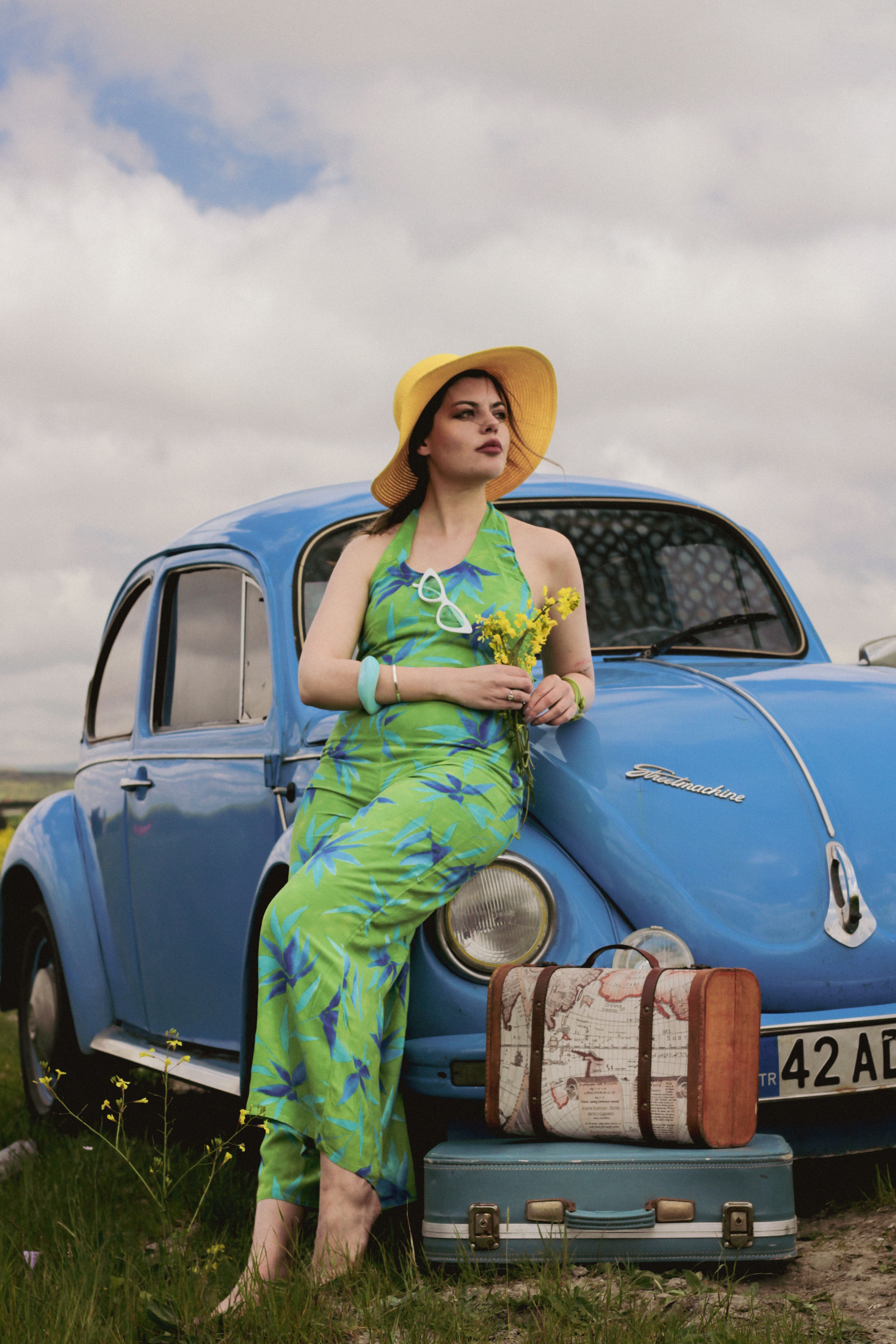 Stylish woman in a summer dress leaning on a vintage car in the countryside.