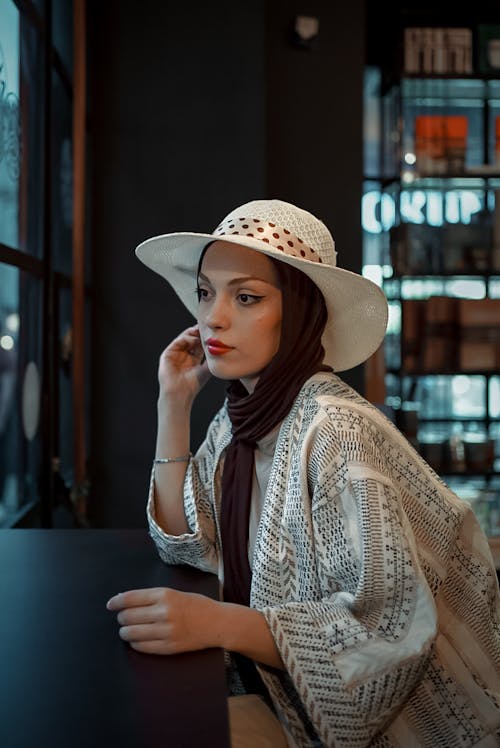 Woman in Hat and Hijab Sitting by Table