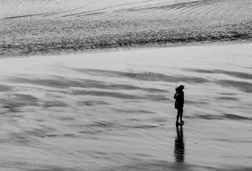 Free A lone woman walks along a serene, monochrome beach shore, evoking solitude. Stock Photo
