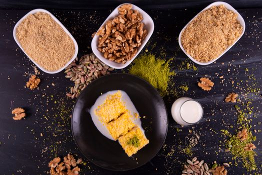 Flat lay of a nutty dessert with walnuts, pistachios, and a glass of milk on a dark background.