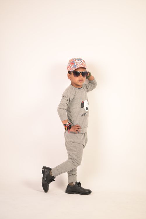 Free A fashionable young boy wearing sunglasses and a cap poses confidently in a gray outfit. Stock Photo