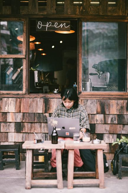 Asian woman working on a laptop in a rustic coffee shop setting. Perfect for depicting remote work.