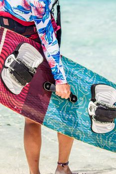 A surfer holds a colorful wakeboard at a sunny beach, ready for the waves.