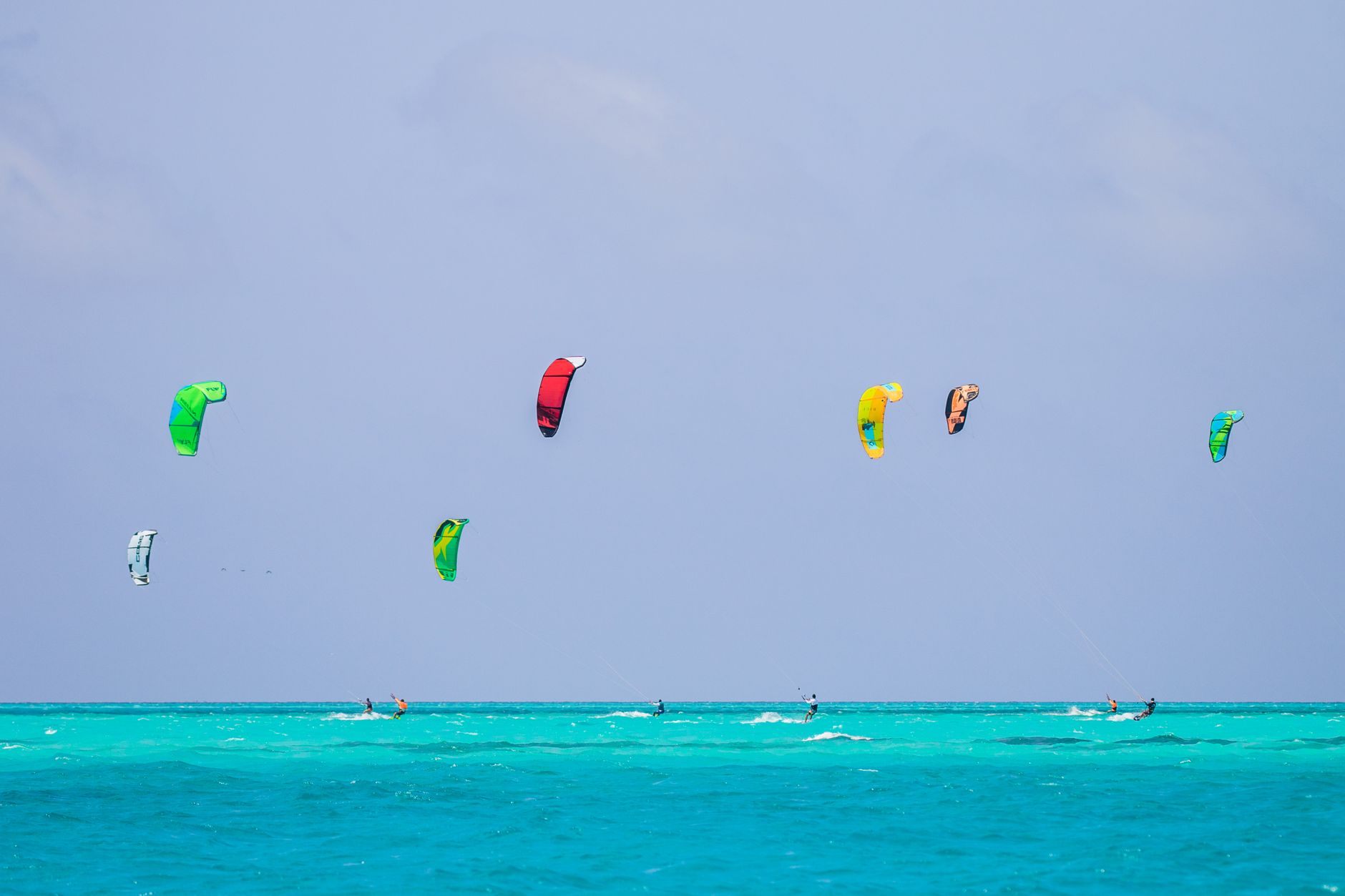 Kiteboarders enjoying a bright summer day on the vibrant turquoise sea with colorful kites.