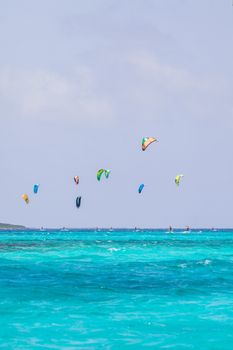 Energetic kitesurfers fly colorful kites over a turquoise ocean under a clear sky, conveying adventure and summer vibes.