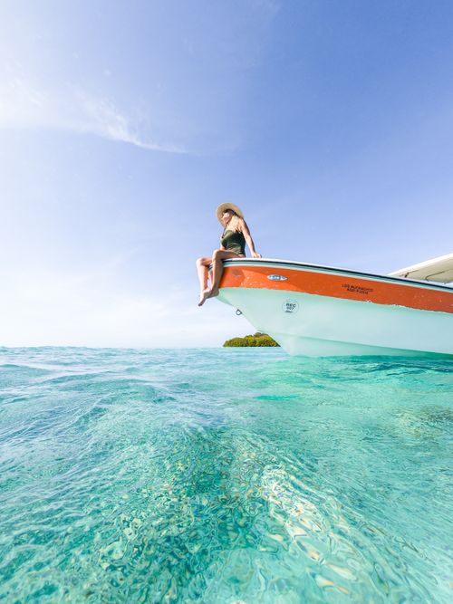 Free Woman enjoying a sunny day on a yacht in turquoise waters, epitomizing a relaxing summer vacation. Stock Photo