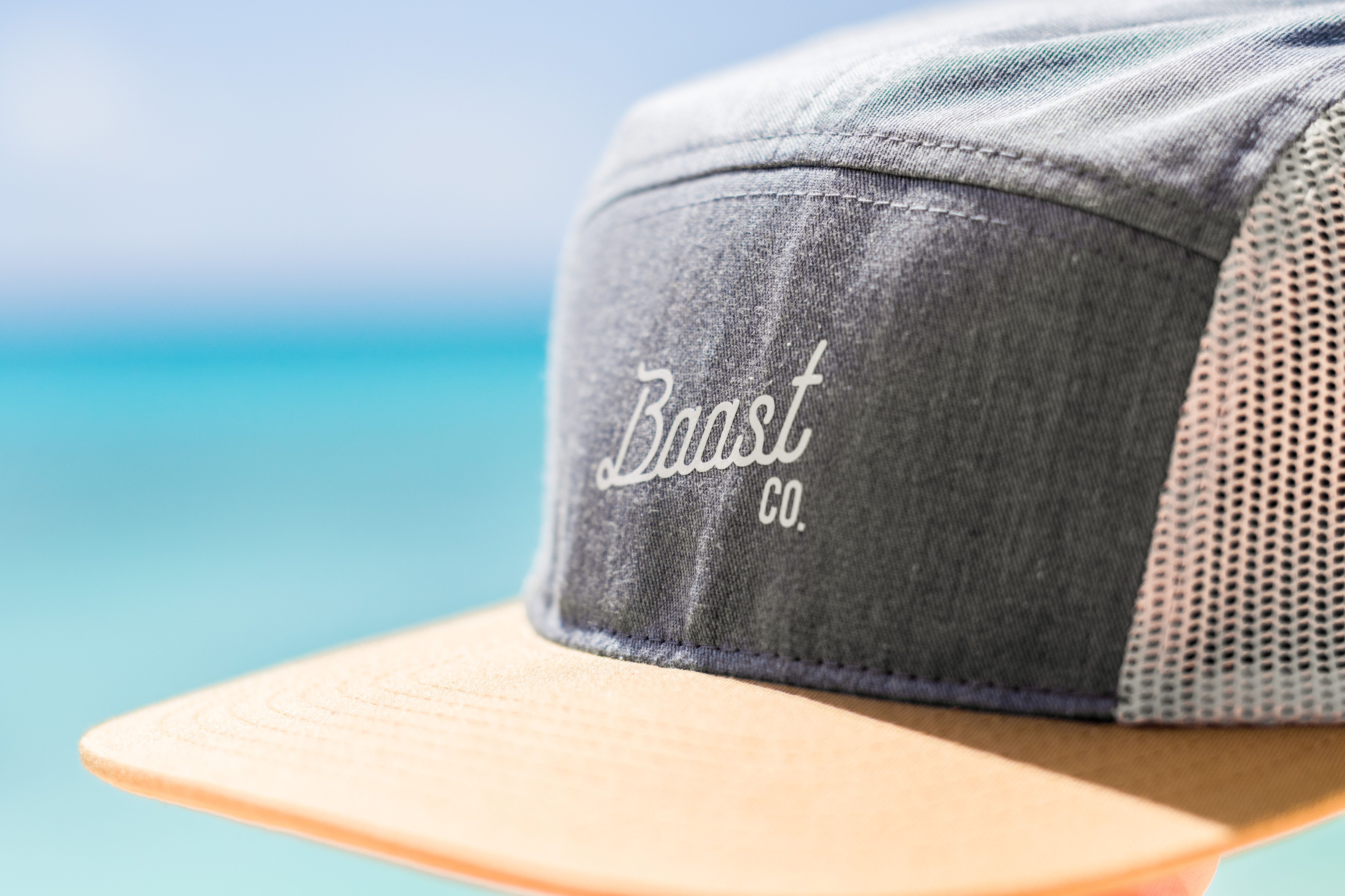 Close-up of a gray Baast Co baseball cap with a yellow visor on a sunny day.