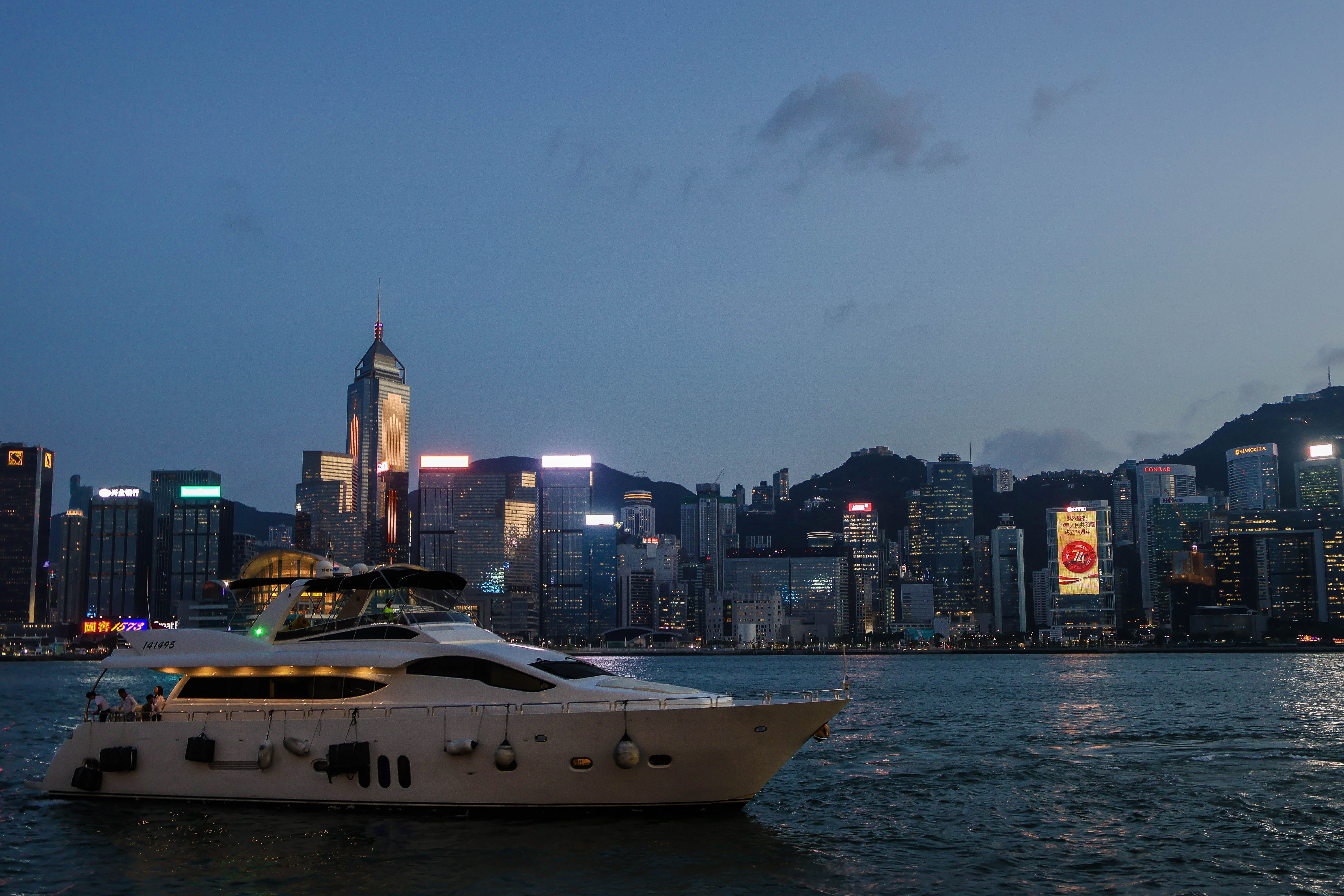 A stunning view of a luxurious yacht sailing near Hong Kong's illuminated skyline during twilight.