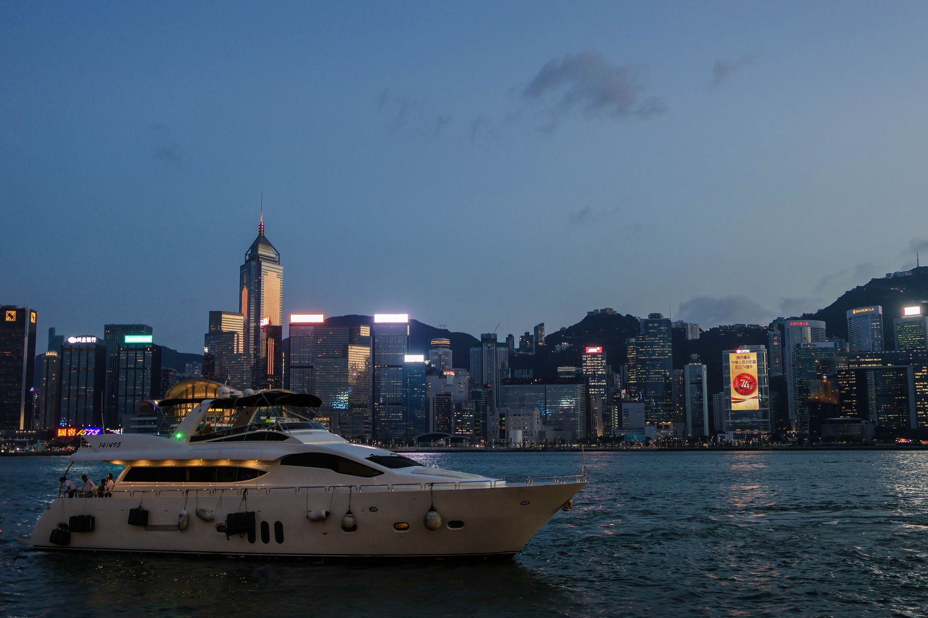 A stunning view of a luxurious yacht sailing near Hong Kong's illuminated skyline during twilight.