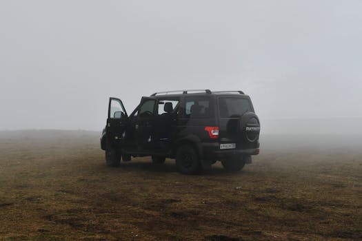 Black SUV parked on a foggy grassland, doors open, amidst a misty rural backdrop.