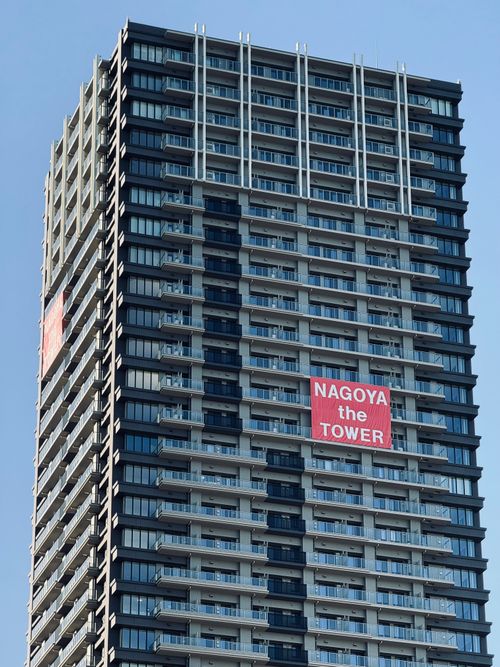 Free A close-up view of a modern skyscraper labeled 'Nagoya the Tower' under a clear blue sky. Stock Photo