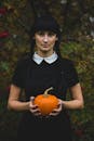 秋天的户外，一名身穿黑色连衣裙的年轻女子拿着南瓜