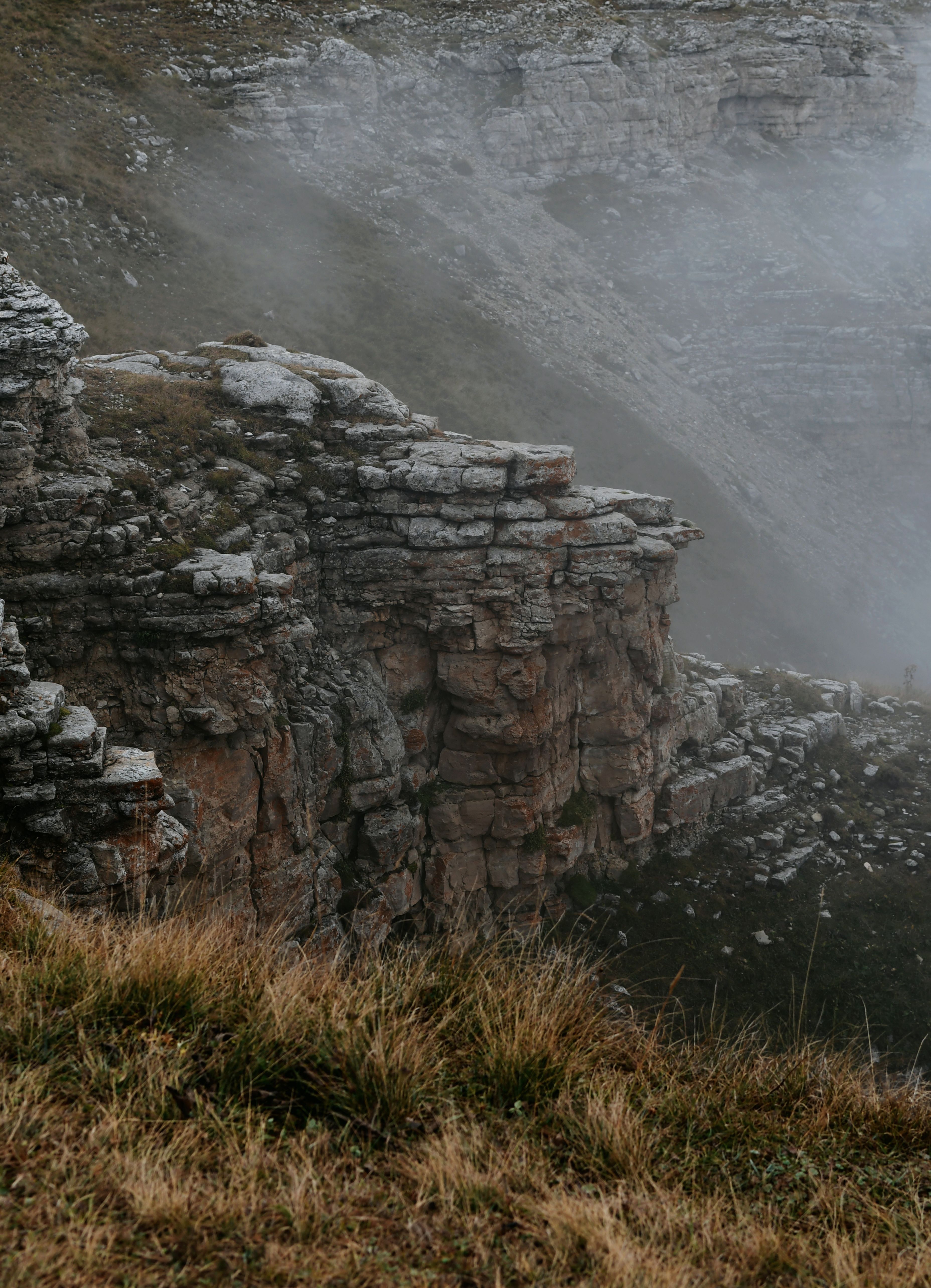 Eroded foggy cliff with rugged rock formations in a misty atmosphere.