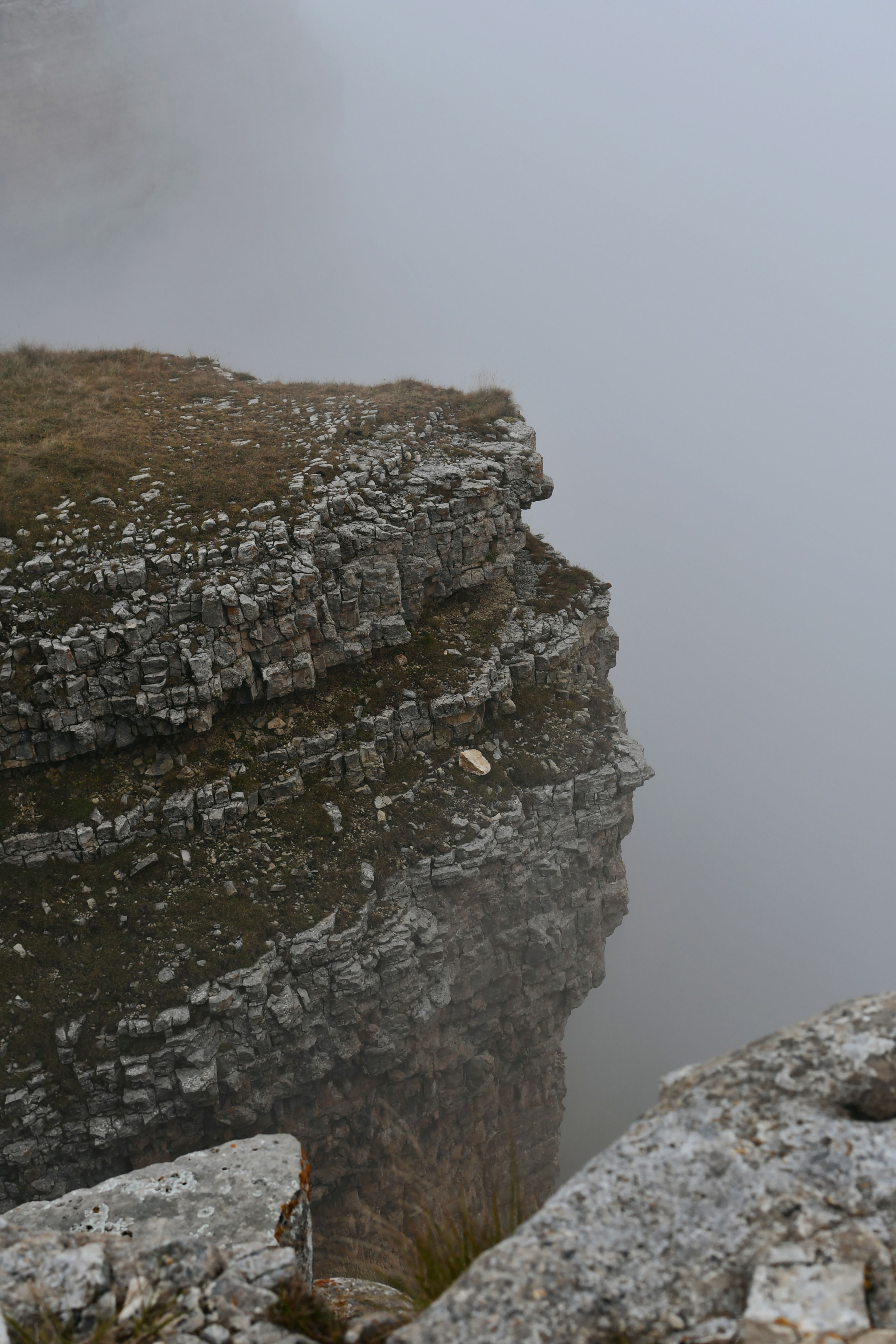 A dramatic view of a rocky cliff shrouded in dense fog, evoking a mysterious and moody atmosphere.