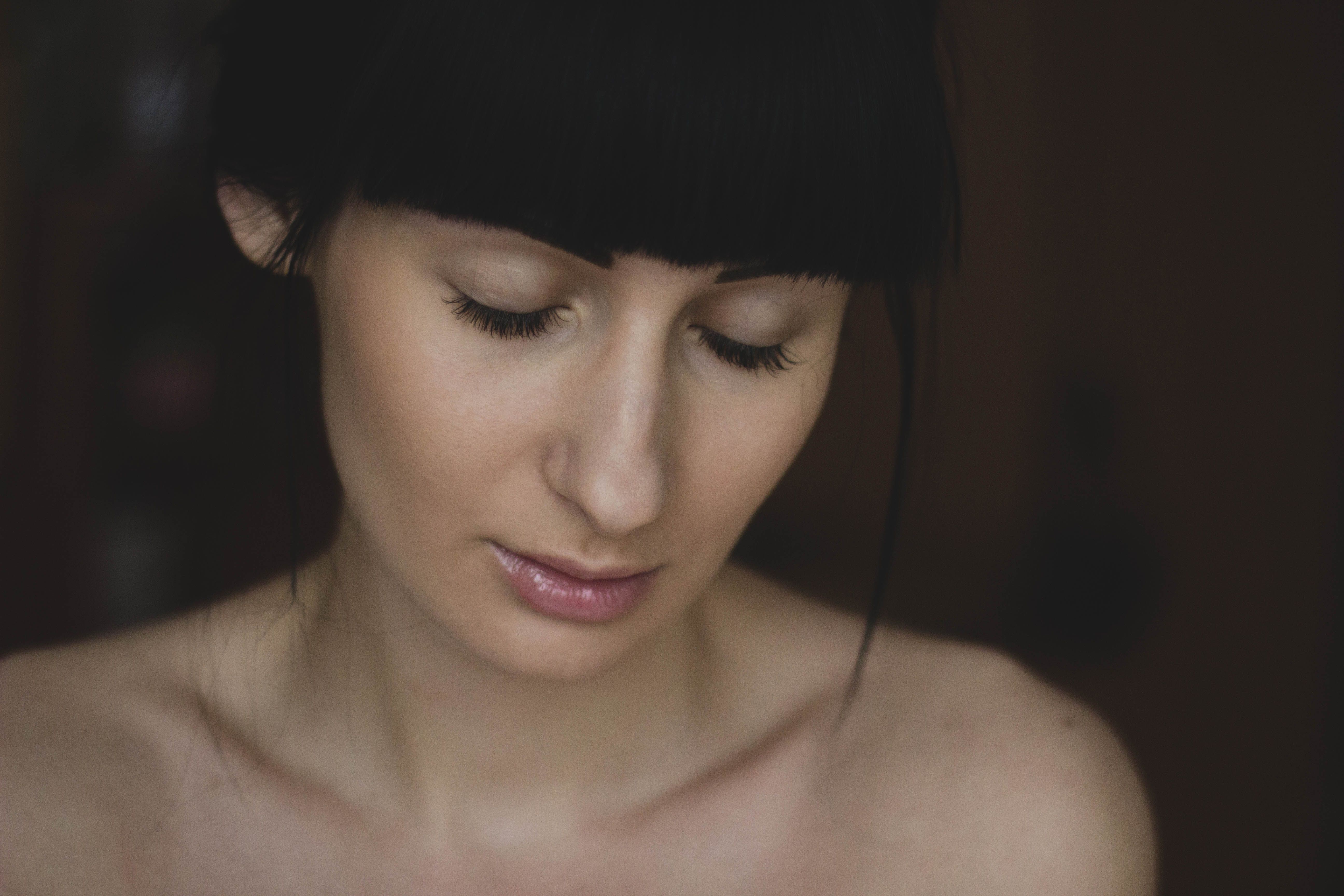 Close-up of a woman with dark hair and serene expression, eyes cast downwards.