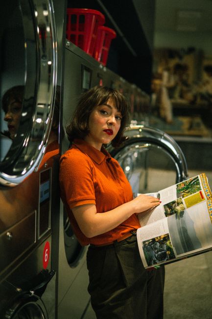 A woman reads a magazine while waiting at a modern laundromat with washing machines.