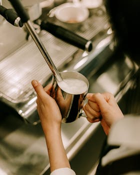 Barista steaming milk for coffee in a cozy café setting, captured with a warm and inviting tone.