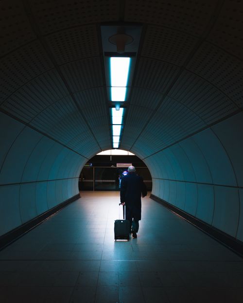Free A man walks through a dimly lit urban tunnel with a suitcase, showcasing modern travel. Stock Photo