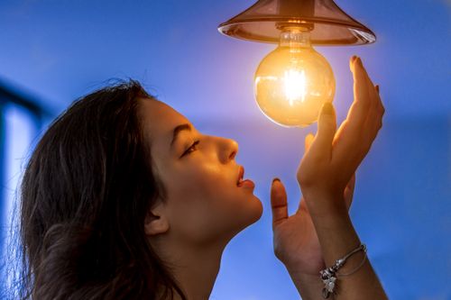 Free Side profile of a woman gazing at a glowing light bulb, creating a warm and captivating atmosphere. Stock Photo