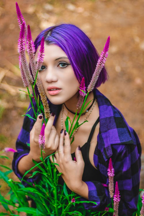 紫色的花朵旁邊的紫色和黑色格子領襯衫的紫色頭髮的女人的照片