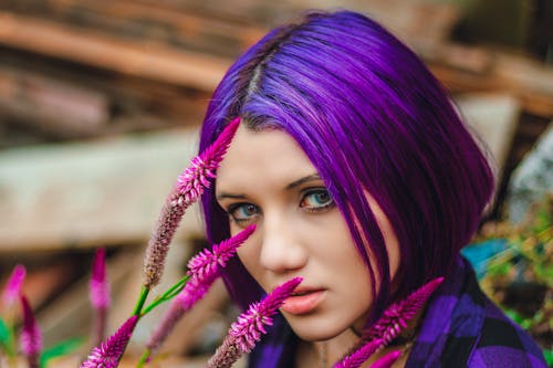 Photo of Purple Haired Woman in Purple and Black Plaid Collared Shirt Next to Purple Flowers
