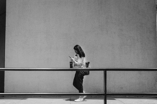 Free Black and white photo of a woman walking with a smartphone against a large concrete wall. Stock Photo