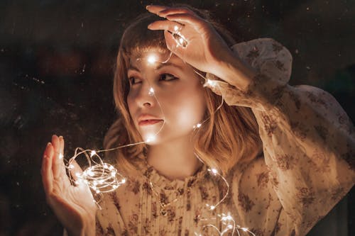 Photo of Woman in White Floral Dress Holding Turned-on String Lights