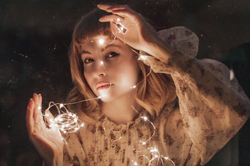 Photo of Woman in White Floral Dress Holding Turned-on String Lights