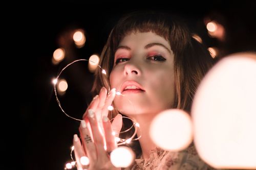 Free Artistic portrait of a young woman holding string lights, creating a magical, dreamy effect. Stock Photo