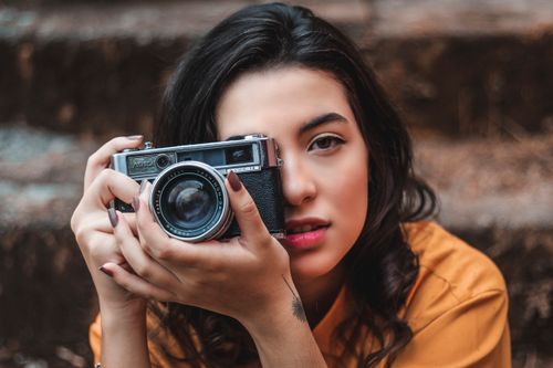 Free Portrait of a stylish young woman holding a vintage camera outdoors. Stock Photo