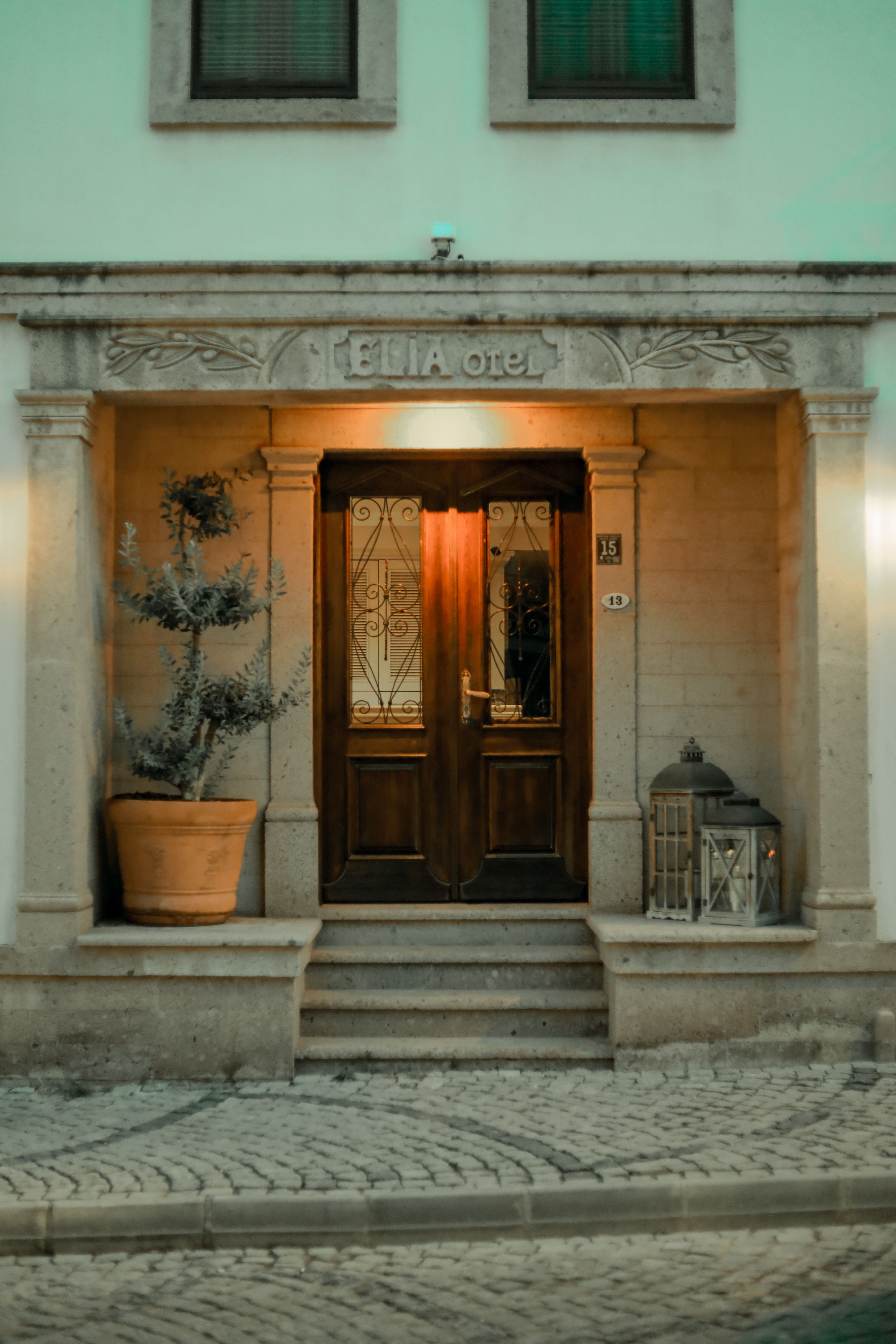 Warmly illuminated hotel entrance with ornate doors and potted plants, creating a cozy ambiance.
