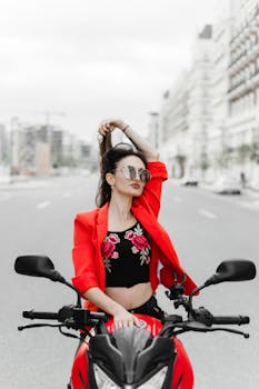 Stylish woman in red posing on a motorbike, urban backdrop in Baku, Azerbaijan.