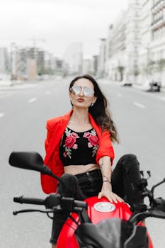 A fashionable woman in a red jacket poses on a motorcycle in an urban street of Baku, Azerbaijan.