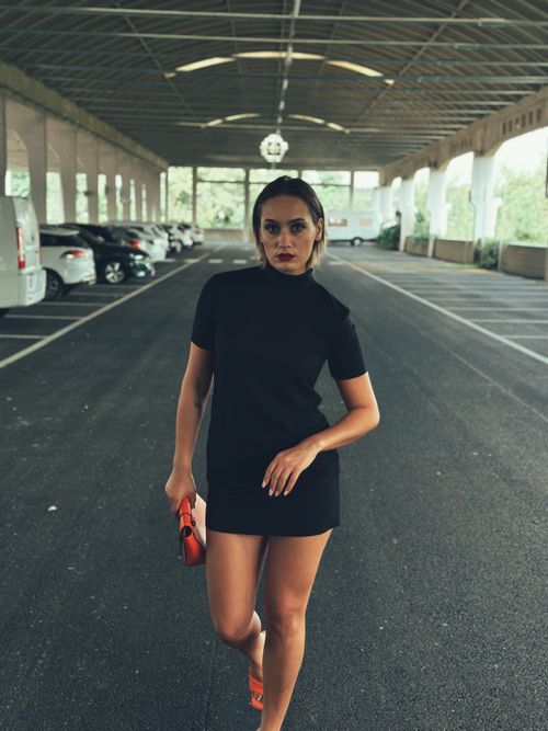 Free Stylish woman posing in black dress at urban parking lot, capturing a modern city vibe. Stock Photo