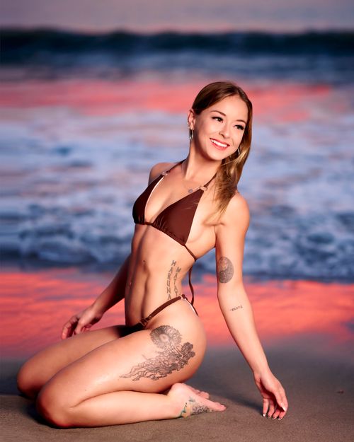Free A woman in a bikini poses on the beach at sunset, showcasing tattoos. Stock Photo