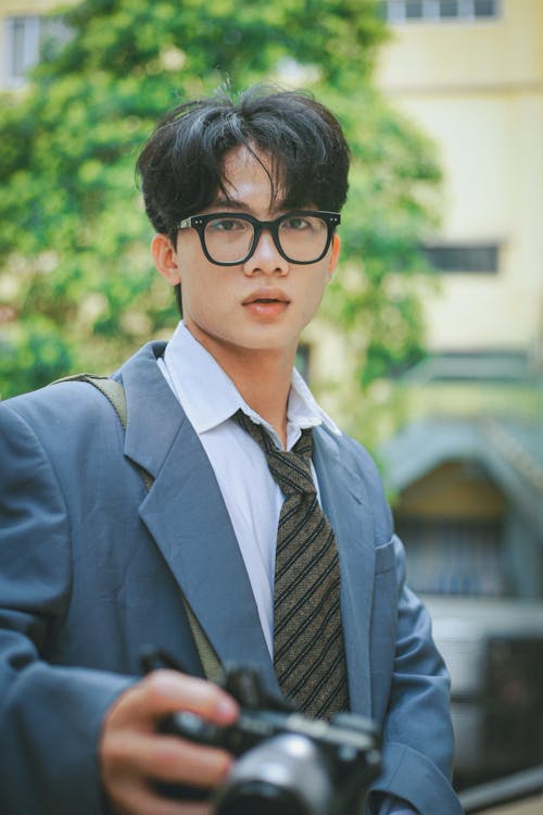 Young Man in Elegant Blue Blazer and Eyeglasses Holding a Photo Camera