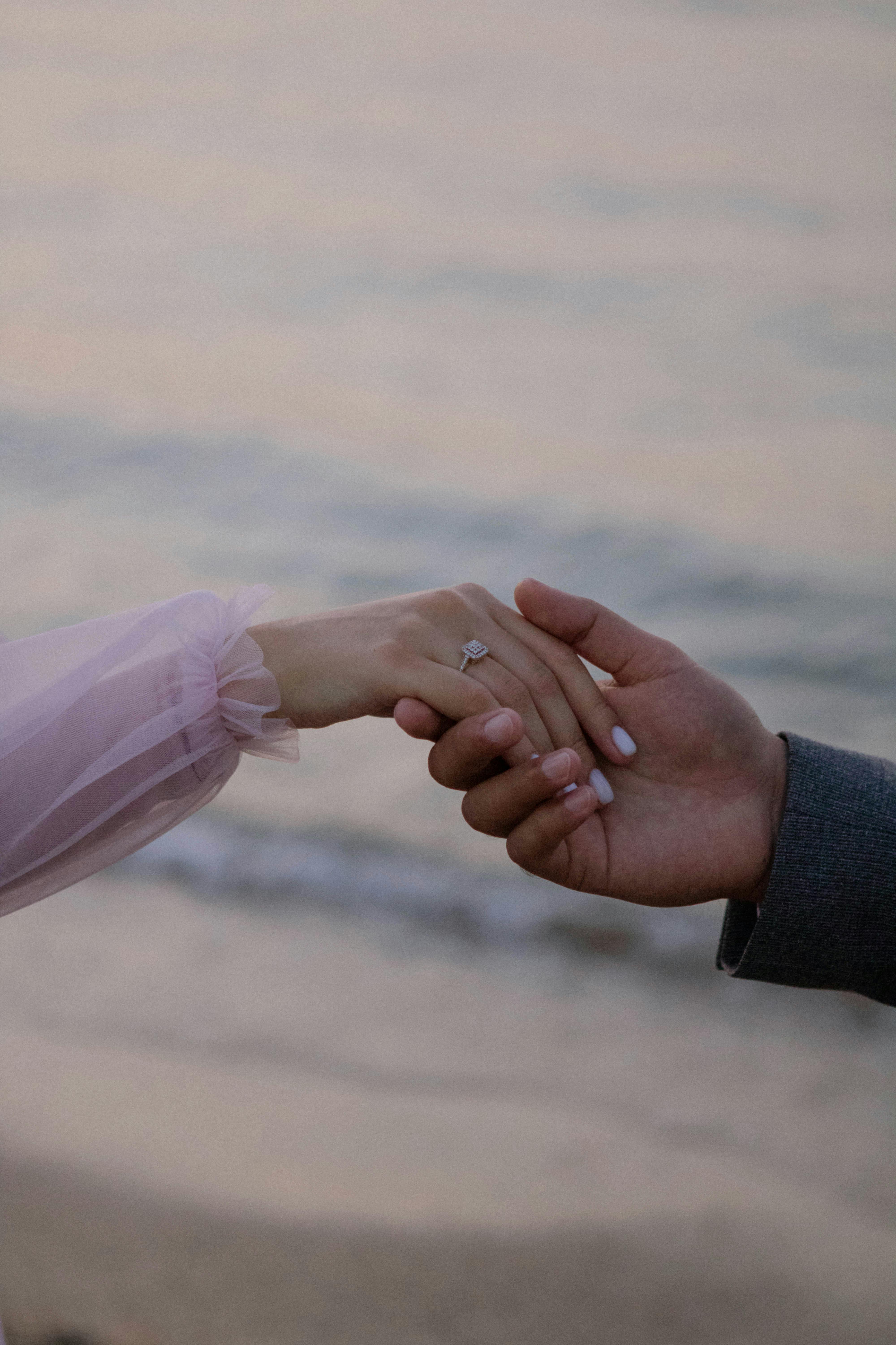 Couple holding hands with engagement ring by the waters of Baku, Azerbaijan at sunrise.