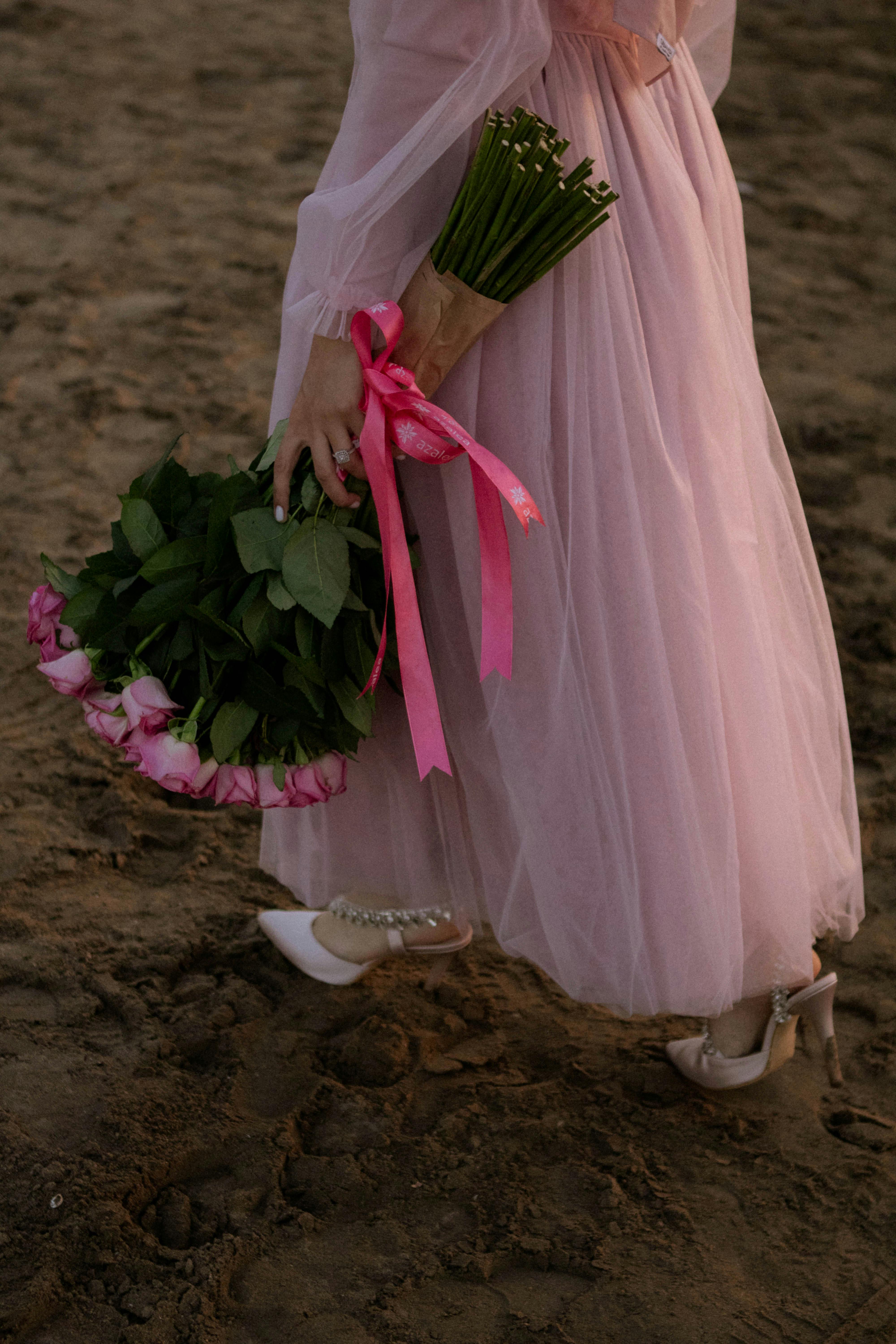 Woman in pink dress holding rose bouquet on sandy beach. Romantic and elegant scene in Baku.
