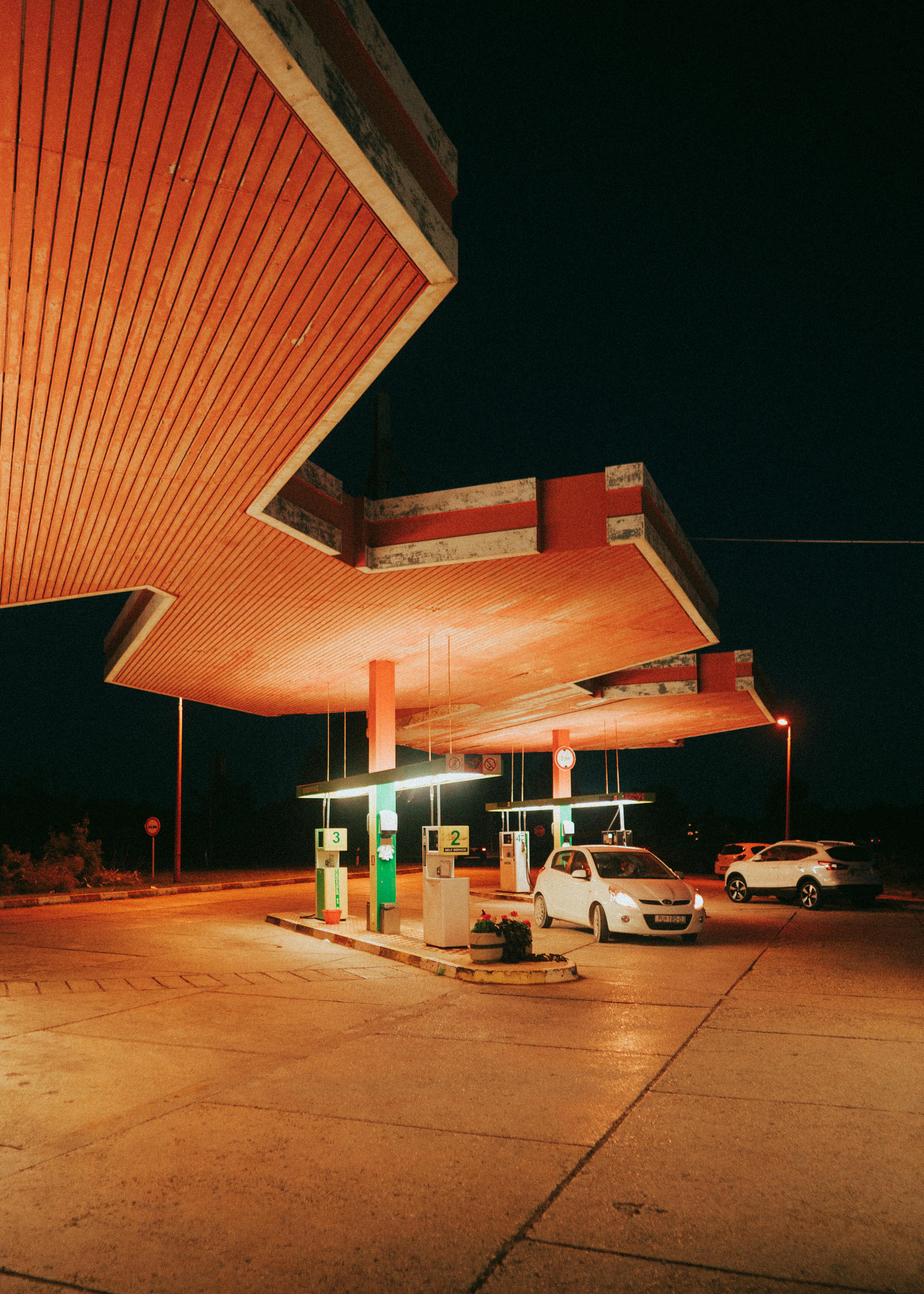 A vintage illuminated gas station with cars under canopy during nighttime, evoking a retro vibe.