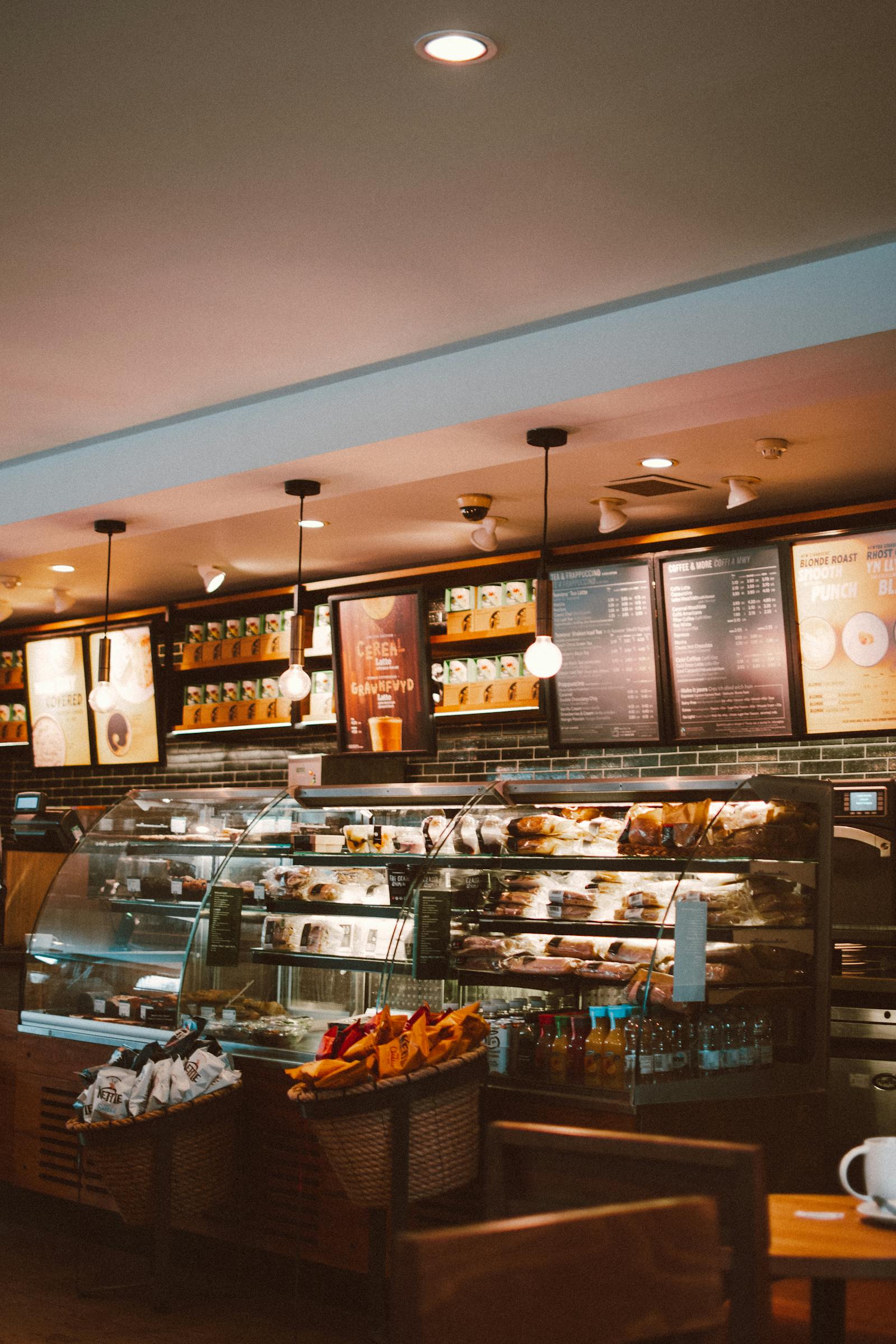 Modern café interior with a glass bakery case, hanging lights, and coffee menu boards—highlighting local dining and coffee shop convenience near Arbor Creek in Saskatoon.