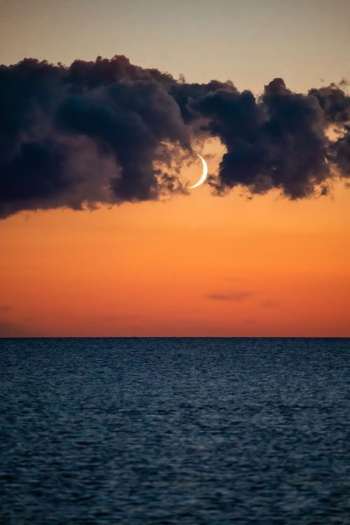 Free Serene crescent moon at dusk glowing above tranquil sea in Amrum, Germany. Stock Photo