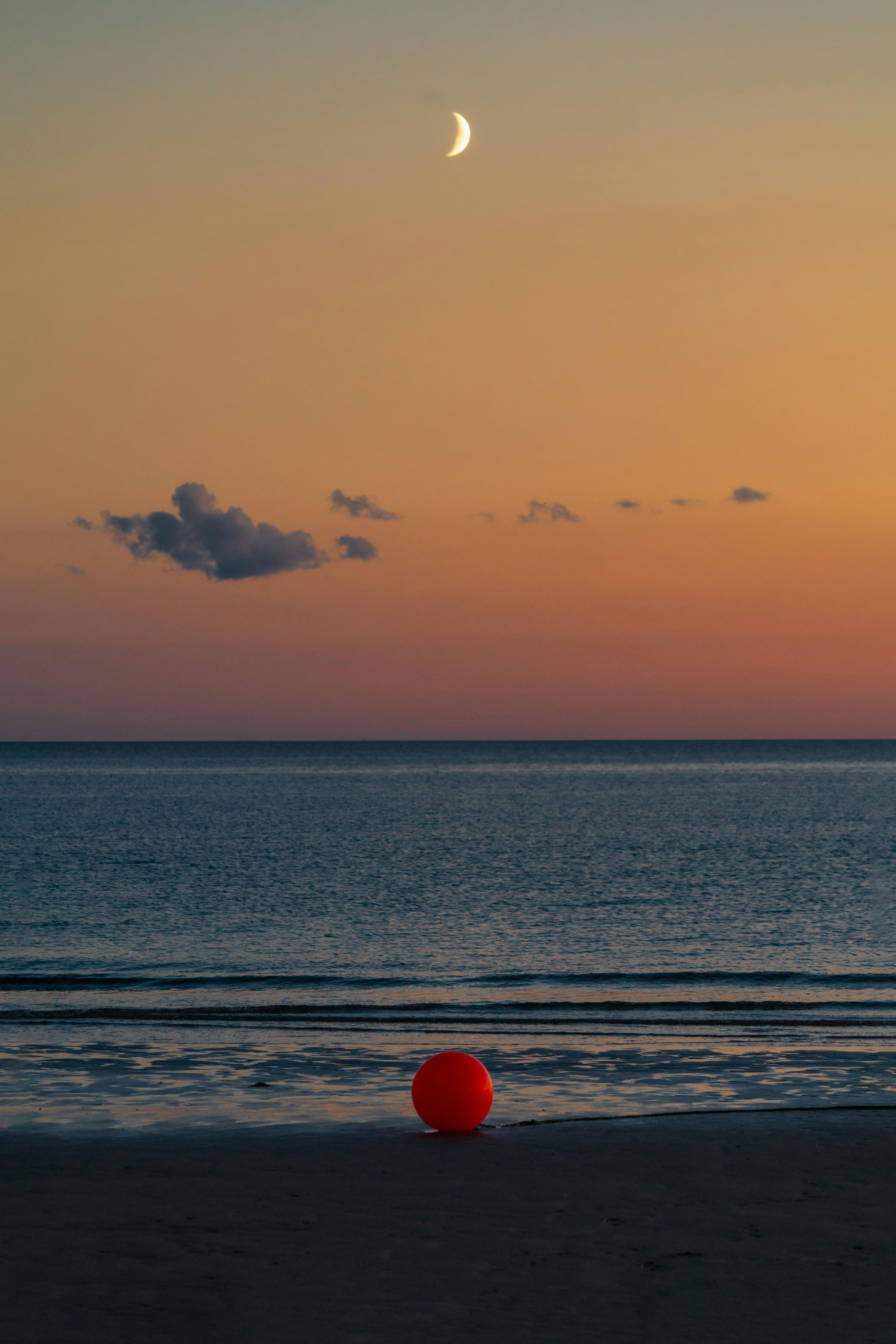 Tranquil beach with crescent moon and red buoy at twilight in Wittdün auf Amrum, Germany.